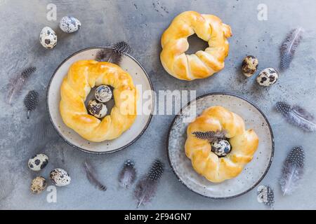 Focaccine pasquali fatte in casa su sfondo grigio, decorate con uova naturali e piume, vista dall'alto Foto Stock