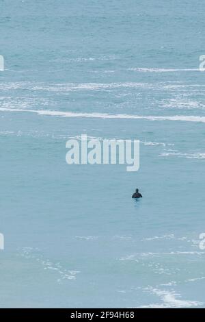 Un surfista in attesa di un'onda in mare calmo a Fistral Bay a Newquay in Cornovaglia. Foto Stock