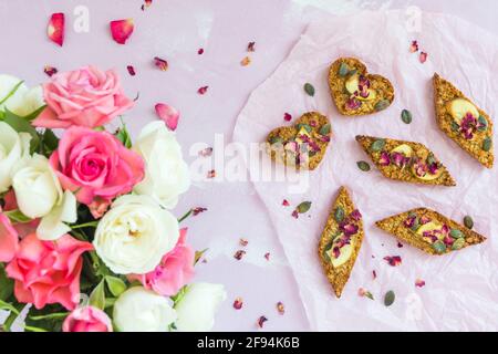 Barrette di muco fatte in casa con mela secca e semi di zucca, adagiate su uno sfondo rosa pallido, decorate con un bouquet di rose rosa e bianche, top Foto Stock