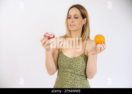 Donna felice che tiene in mano frutta arancione e ciambelle. Vita sana, dieta e concetto di nutrizione. Foto Stock