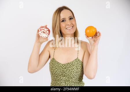 Donna felice che tiene in mano frutta arancione e ciambelle. Vita sana, dieta e concetto di nutrizione. Foto Stock