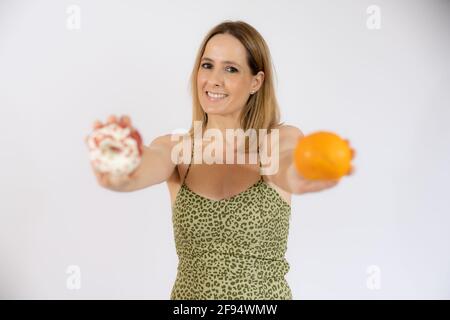 Donna felice che tiene in mano frutta arancione e ciambelle. Vita sana, dieta e concetto di nutrizione. Foto Stock