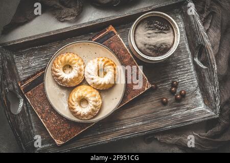 Tre mini torte fatte in casa su un piatto, una tazza di caffè e un vecchio libro su un vassoio di legno su sfondo grigio, vista dall'alto Foto Stock