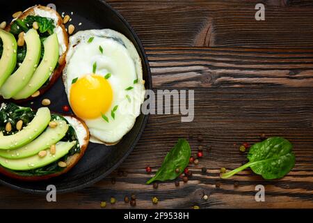 In una padella, inzidire con avocado, spinaci e uova fritte. Sfondo rustico di legno scuro e posto per un'iscrizione. Vista dall'alto. Foto Stock