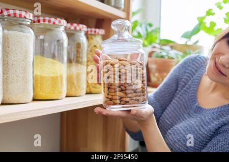 Casa dispensa cucina interno, donna che tiene vaso di mandorle Foto Stock