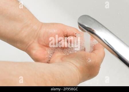 L'uomo anziano le lava le mani sotto il rubinetto in bagno, raccomandazione per frequenti lavaggi delle mani, igiene domestica. Foto Stock