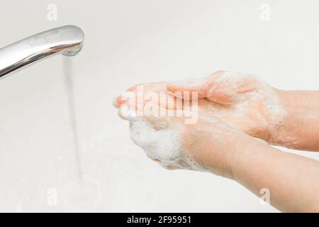 La donna anziana le lava le mani con sapone sotto il rubinetto in bagno, la raccomandazione di lavarsi le mani frequentemente. Igiene domestica. Foto Stock