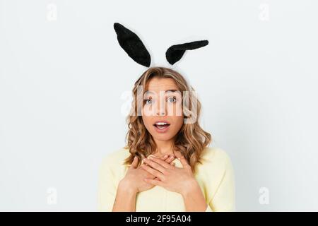 Sorpresa eccitato giovane donna che indossa orecchie coniglietto di pasqua guardando la fotocamera non può credere ciò che ha sentito, bianco sfondo studio. Foto Stock