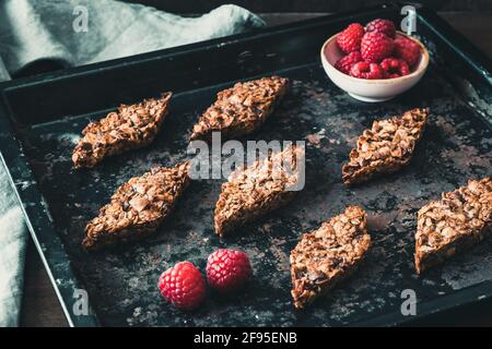 Barrette fatte in casa con lamponi in granola, decorate con lamponi, adagiate su una teglia scura Foto Stock