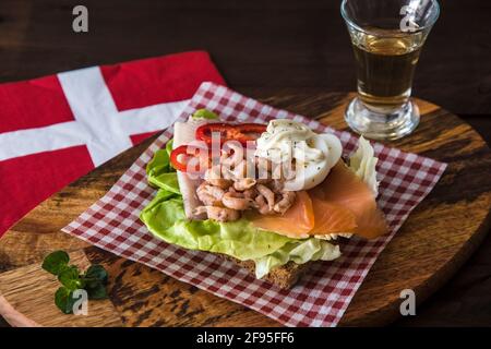 Panino danese con salmone, kipper e granchi giacenti su un tovagliolo rosso-bianco controllato su una tavola di legno Foto Stock