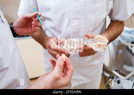 Medici dentisti in piedi in ufficio, clinica con una sedia, strumenti. Luogo di lavoro del dentista. Gli ortodontisti tengono in mano ed esaminano il getto della mascella Foto Stock