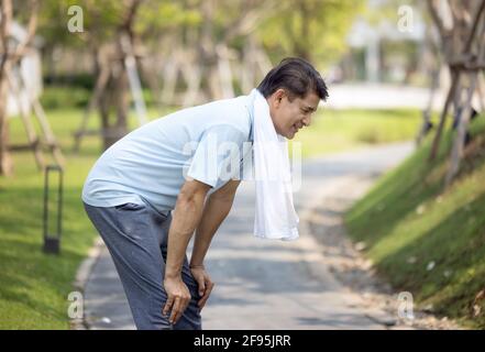 ritratto di sano sportivo maschio maturo in felpa con cappuccio e scarpe da running che si esercitano all'aperto, pratica affondo laterali. Uomo anziano sopportato in sportswear caldo Foto Stock