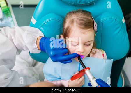 Un medico professionista, un dentista per bambini, tratta i denti di una bambina con strumenti. Studio dentistico per esame paziente. Il processo di ammaccatura Foto Stock