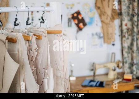 Molti modelli di cucitura della carta per i vestiti differenti appesi sul rack nello sfondo della fabbrica di cucitura. Modello di abbigliamento, fabbricazione in fabbrica di cucito Foto Stock