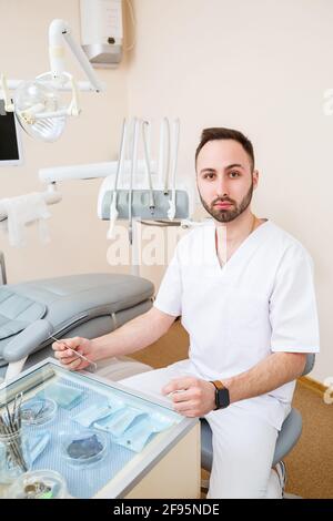 Dentista sul posto di lavoro. Medico allegro in un ufficio spazioso e moderno e guardando la macchina fotografica con un sorriso gentile Foto Stock