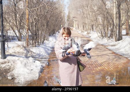 Una donna alimenta i piccioni in un parco cittadino Foto Stock