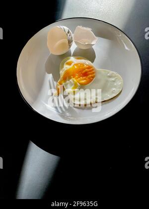 Uova fritte sotto forma di cuore su un piastra bianca con conchiglie Foto Stock