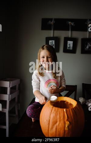 Ragazza che intagliano la zucca e che scopano i semi sulla sua cucina tavolo a casa Foto Stock