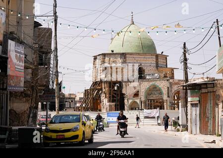 Un uomo che guida una moto vicino alla Moschea al-Nuri. La Moschea al-Nuri fu costruita nel 1,172 e che comprende anche il minareto di al-Hadba, è attualmente in fase di ricostruzione nel suo vecchio progetto da parte dell'UNESCO dopo essere stata distrutta durante la guerra contro l'Isis (Stato islamico dell'Iraq e della Siria). La moschea ebbe un significato simbolico per l'Isis, poiché il suo leader, Abu Bakr al-Baghdadi, dichiarò il cosiddetto califfato dall'interno della moschea. Foto Stock