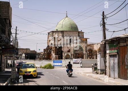 Un uomo che guida una moto vicino alla Moschea al-Nuri. La Moschea al-Nuri fu costruita nel 1,172 e che comprende anche il minareto di al-Hadba, è attualmente in fase di ricostruzione nel suo vecchio progetto da parte dell'UNESCO dopo essere stata distrutta durante la guerra contro l'Isis (Stato islamico dell'Iraq e della Siria). La moschea ebbe un significato simbolico per l'Isis, poiché il suo leader, Abu Bakr al-Baghdadi, dichiarò il cosiddetto califfato dall'interno della moschea. Foto Stock