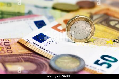 Una moneta da 1 euro usata in cima ad alcune banconote in euro. Economia e finanza nell'Unione europea. Foto Stock