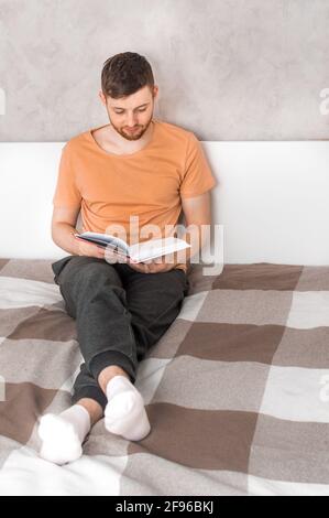 il giovane legge un libro a letto. Verticale. Foto verticale Foto Stock