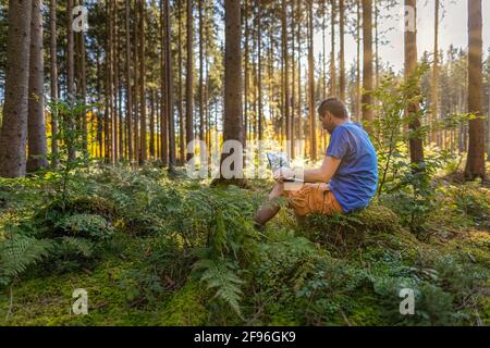 Equilibrio sano della vita lavorativa - uomo che lavora con un computer portatile in una foresta verde all'aria fresca in una foresta. Foto Stock