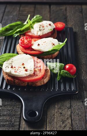 Panini aperti o bruschetta con mozzarella, pomodori e basilico, caprese su sfondo di legno scuro. Foto Stock