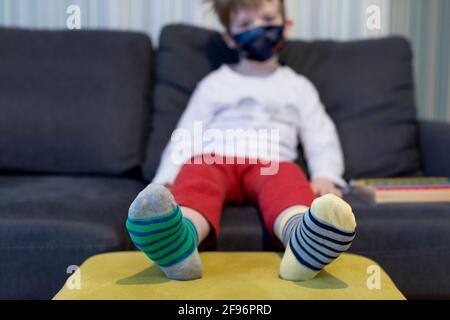 Concetto di consapevolezza della sindrome di Down. Ragazzo che indossa calzini diversi mentre si siede sul divano a casa. Calze diverse come simbolo della sindrome di Down. Focu selettivo Foto Stock