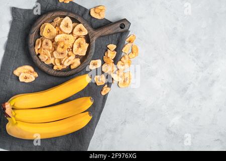 Patatine di banana fatte in casa e banane fresche su sfondo grigio. Vista dall'alto, spazio di copia. Foto Stock