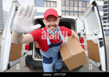 Sorridente corriere maschio che tiene grande scatola di cartone sullo sfondo di auto Foto Stock