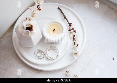 Rami dell'albero di albicocca in fiore in vaso e candela bruciante sopra vassoio rotondo all'interno della casa Foto Stock