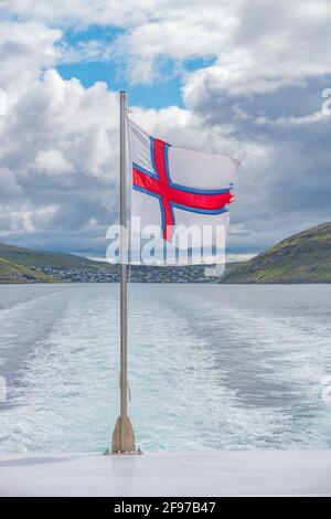 La bandiera nazionale delle Isole Faroe sta balzando nel vento attaccato ad una barca turistica all'arcipelago delle isole Faroe e all'oceano Atlantico, estate Foto Stock
