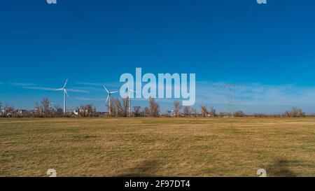 Vista panoramica sul paesaggio agricolo con turbine eoliche per generare energia elettrica verde e cavi elettrici ad alta potenza che attraversano il cielo blu, Magde Foto Stock