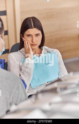 Giovane donna con mal di denti, seduta in una sedia dentale presso la clinica. Paziente femminile con tremendo mal di denti in visita dentista. Foto Stock