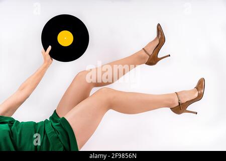 Gambe donna irriconoscibili con tacchi alti che tengono un disco in vinile su wh Foto Stock