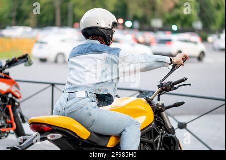 Colpo posteriore destro di una giovane donna che cavalca un giallo moto Foto Stock