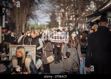 BELGRADO, SERBIA - 21 FEBBRAIO 2021: Sfocatura selettiva su una giovane donna che indossa una maschera facciale in una strada affollata con persone che siedono nei caffè di Zemun Foto Stock