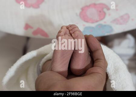 Primo piano di una persona che tiene i piedi di un neonato un letto con sfondo sfocato Foto Stock