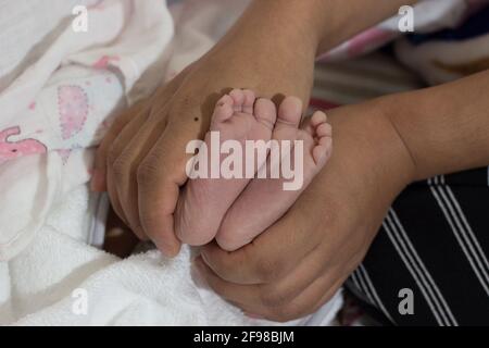 Primo piano di una persona che tiene i piedi di un neonato un letto con sfondo sfocato Foto Stock