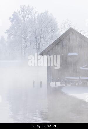 Una magica mattinata invernale alle boathouses di Schlehdorf am Kochelsee, Baviera, con brina, sole, nebbia e neve fresca caduta. Foto Stock