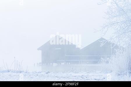 Una magica mattinata invernale alle boathouses di Schlehdorf am Kochelsee, Baviera, con brina, sole, nebbia e neve fresca caduta. Foto Stock