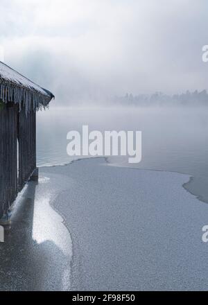 Una magica mattinata invernale alle boathouses di Schlehdorf am Kochelsee, Baviera, con brina, sole, nebbia e neve fresca caduta. Foto Stock