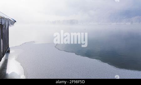 Una magica mattinata invernale alle boathouses di Schlehdorf am Kochelsee, Baviera, con brina, sole, nebbia e neve fresca caduta. Foto Stock