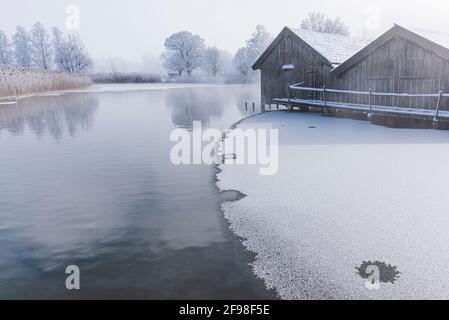 Una magica mattinata invernale alle boathouses di Schlehdorf am Kochelsee, Baviera, con brina, sole, nebbia e neve fresca caduta. Foto Stock