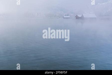 Una magica mattinata invernale alle boathouses di Schlehdorf am Kochelsee, Baviera, con brina, sole, nebbia e neve fresca caduta. Foto Stock