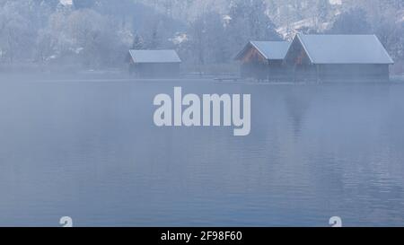 Una magica mattinata invernale alle boathouses di Schlehdorf am Kochelsee, Baviera, con brina, sole, nebbia e neve fresca caduta. Foto Stock