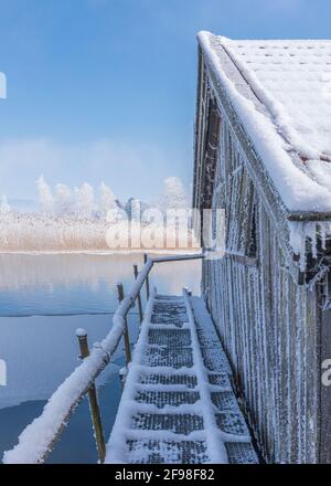 Una magica mattinata invernale alle boathouses di Schlehdorf am Kochelsee, Baviera, con brina, sole, nebbia e neve fresca caduta. Foto Stock