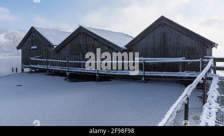 Una magica mattinata invernale alle boathouses di Schlehdorf am Kochelsee, Baviera, con brina, sole, nebbia e neve fresca caduta. Foto Stock