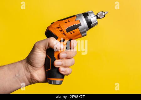 Mano di un uomo sconosciuto che tiene un cacciavite elettrico - presa maschio attrezzatura da lavoro su sfondo giallo brillante - ristrutturazione riparazione strumenti per apparecchiature elettriche Foto Stock